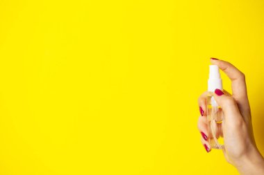 Bir kadın sarı arka planda antiseptik kullanıyor.