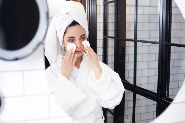 Mujer linda en abrigo blanco y toalla en su cabeza se hace un maquillaje — Foto de Stock