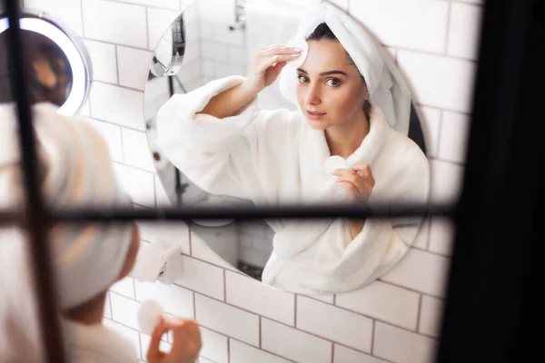 Mujer linda en abrigo blanco y toalla en su cabeza se hace un maquillaje — Foto de Stock