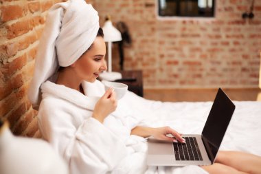 Sevimli kadın evde kalıp laptopta çalışıyor ve kahve içiyor.