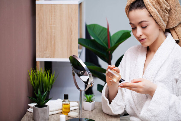 Милая женщина в ванной комнате делает косметическую процедуру для ухода за кожей лица
