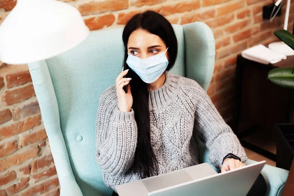 Pretty woman in mask on her face working on laptop at home during pandemic — Stock Photo, Image