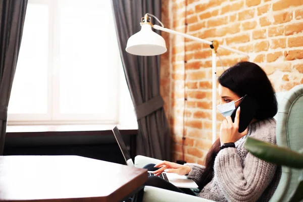 Pretty woman in mask on her face working on laptop at home during pandemic — Stock Photo, Image