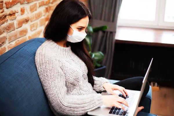 Pretty woman in mask on her face working on laptop at home during pandemic — Stock Photo, Image