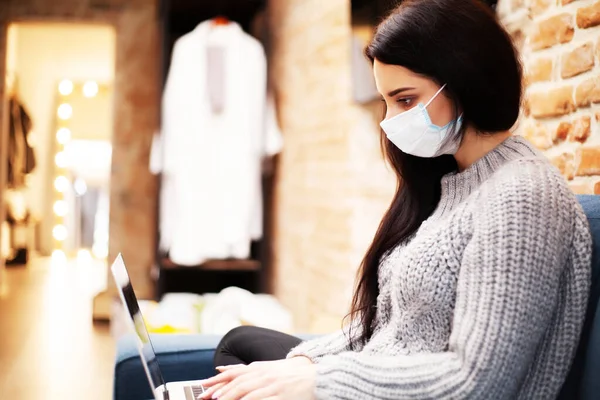 Pretty woman in mask on her face working on laptop at home during pandemic — Stock Photo, Image