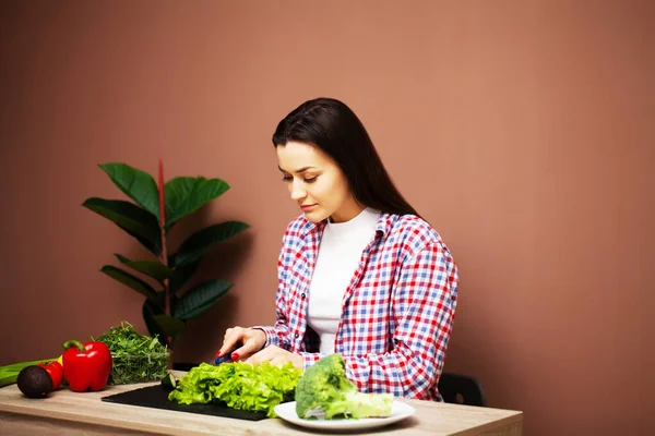 Vacker kvinna förbereder en sallad med färska grönsaker hemma i köket — Stockfoto