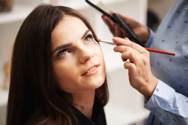 Chica bonita utiliza los servicios de un artista de maquillaje profesional en un estudio de belleza — Foto de Stock