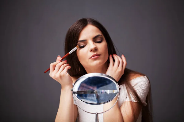 Chica bonita aplica maquillaje en la cara en casa cerca del espejo —  Fotos de Stock