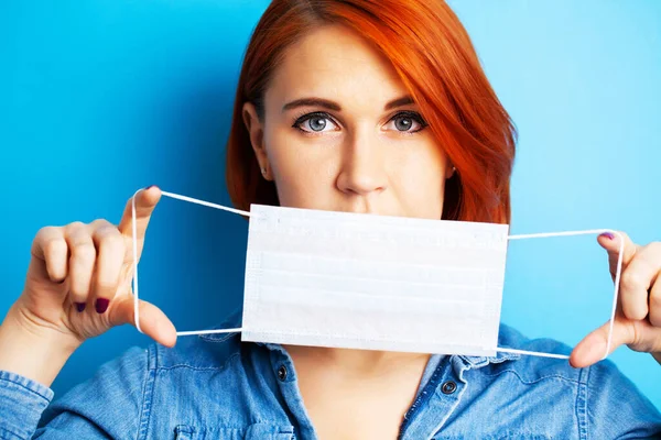 Woman holding mask to cover mouth and nose to protect against virus on blue background