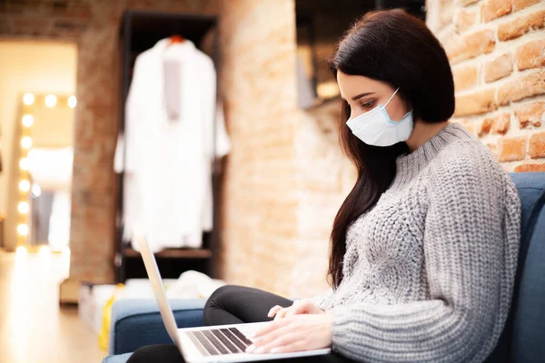Woman in a protective mask works at home on a laptop during a worldwide epidemic of a virus. — Stock Photo, Image