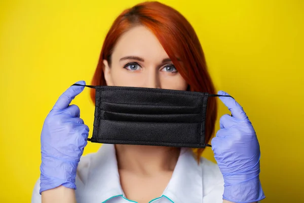 Woman holding mask to cover mouth and nose to protect against virus on yellow background.