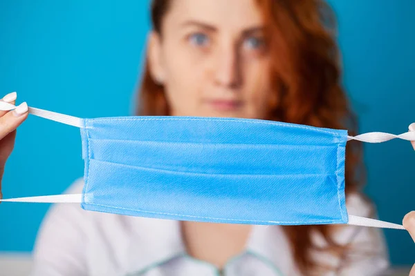 Woman holding mask to cover mouth and nose to protect against virus on blue background