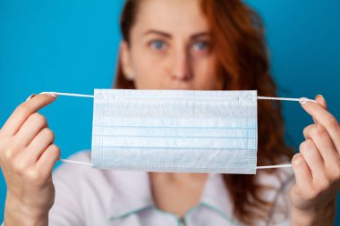 Mavi arka planda virüse karşı korunmak için ağzı ve burnunu gizlemek için maske tutan kadın.