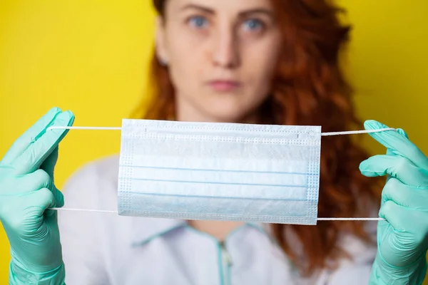 Woman holding mask to cover mouth and nose to protect against virus on yellow background