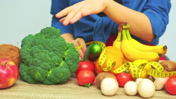 Ung kvinna på en strikt diet på bakgrunden av färska grönsaker och frukter — Stockvideo