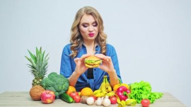Sıkı diyette olan genç bir kadın elinde taze sebze ve meyvelerden oluşan zararlı bir hamburger tutuyor.