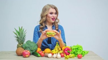 Sıkı diyette olan genç bir kadın elinde taze sebze ve meyvelerden oluşan zararlı bir hamburger tutuyor.