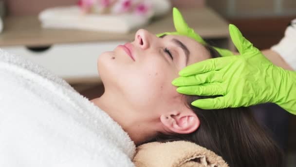 Joven hermosa mujer asiste al spa y recibe masaje facial — Vídeos de Stock