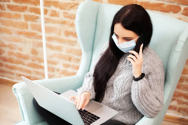 Woman in a protective mask works at home on a laptop during a worldwide epidemic of a virus — Stock Photo, Image