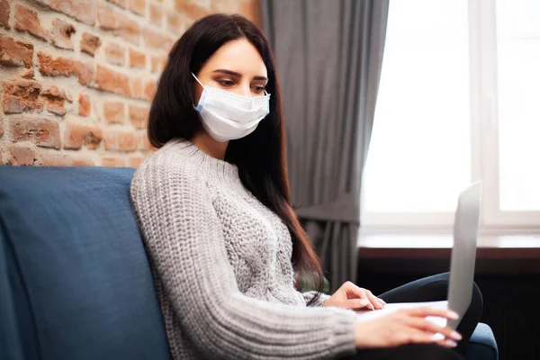 Woman in a protective mask works at home on a laptop during a worldwide epidemic of a virus — Stock Photo, Image