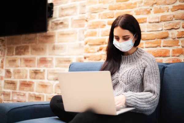 Woman in a protective mask works at home on a laptop during a worldwide epidemic of a virus — Stock Photo, Image