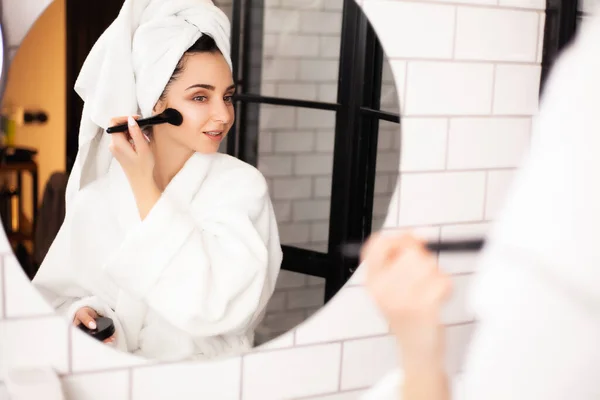 Mujer en el baño con una toalla en la cabeza se pone maquillaje en la cara — Foto de Stock