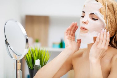 Aynanın önündeki güzel kadın cilt bakımı için yüzüne maske takıyor.