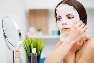 Aynanın önündeki güzel kadın cilt bakımı için yüzüne maske takıyor.