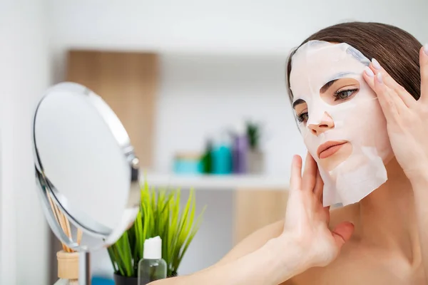Wanita cantik di depan cermin menempatkan masker di wajah untuk perawatan kulit — Stok Foto