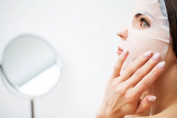 Mulher bonita na frente do espelho coloca uma máscara no rosto para cuidados com a pele — Fotografia de Stock