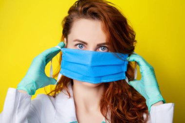 Sarı arka planda virüse karşı korunmak için ağzı ve burnunu gizlemek için maske tutan kadın..