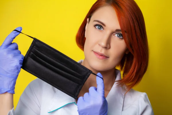 Woman holding mask to cover mouth and nose to protect against virus on yellow background.