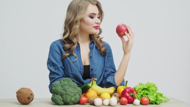 Gezond eten thuis, vrouw in de keuken met verse groenten en fruit op een witte muurachtergrond — Stockvideo
