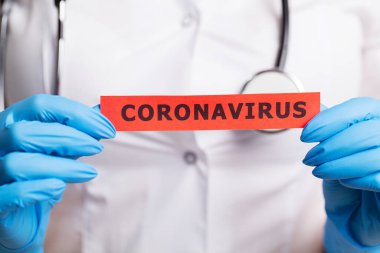 Beyaz önlüklü kadın doktor Coronavirus yazısını tutuyor.