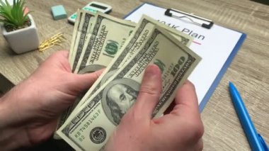 401k emeklilik planı, bir adam tahtadan bir masada 100 dolarlık banknotlar sayar.