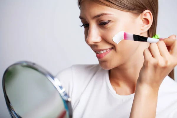 Cosméticos de la piel de la cara de la mujer, mujer delante de un espejo aplica una crema para el cuidado de la piel — Foto de Stock