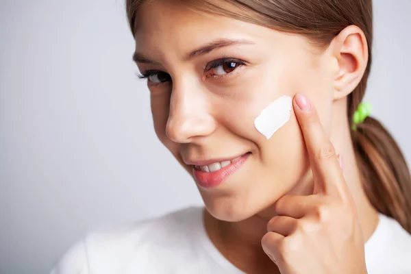 Vrouw gezicht huid cosmetica, vrouw voor een spiegel brengt een crème voor huidverzorging — Stockfoto