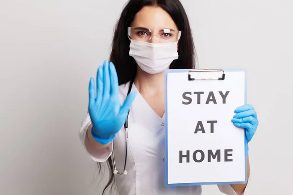 Doctor in a gloves, mask and glasses holds sheet with text stay at home — Stock Photo, Image