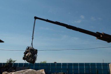 Bir forklift ve işçiler eski bir arabanın motorunu geri dönüşüm için kaldırıyorlar..