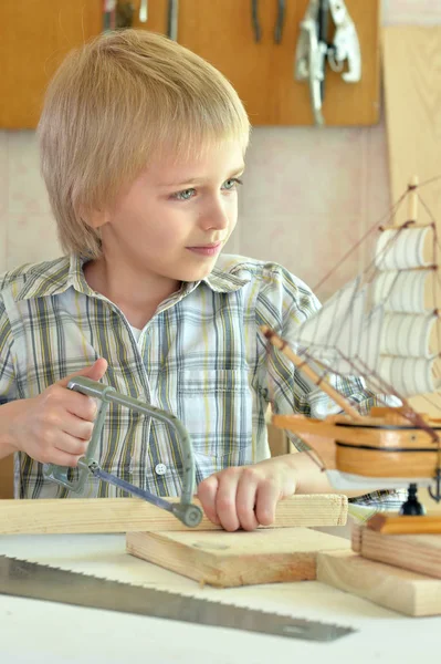 Мальчик с моделью корабля и ручной пилой — стоковое фото