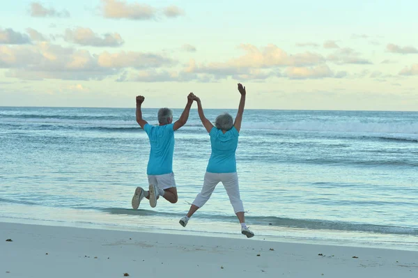 Senior couple jumping on seashore — Stock Photo, Image