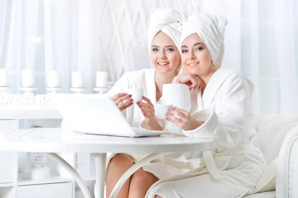 Mujeres jóvenes en albornoces con ordenador portátil — Foto de Stock