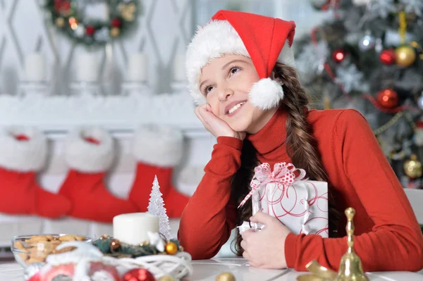 クリスマス プレゼントで座っているサンタ帽子で幸せな少女の肖像画 — ストック写真