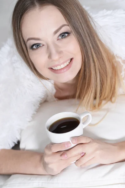 自宅のソファの上のお茶のカップを持つ若い美しい女性 — ストック写真