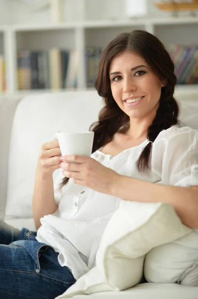 自宅のソファの上のお茶のカップを持つ若い美しい女性 — ストック写真