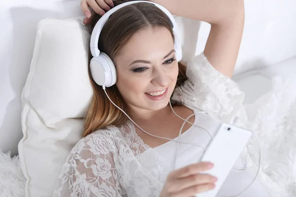年轻美丽的妇女在床上听音乐在家 — 图库照片