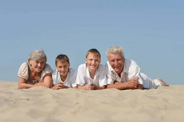 砂の上に休んで自分の孫を持つ祖父母 — ストック写真