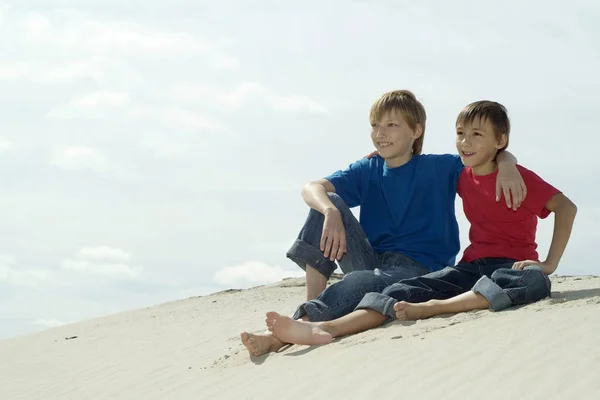 Two cheerful boys sitting  against the sky on sand