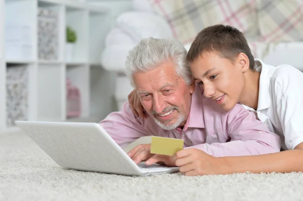 祖父和孙子躺在地板上使用笔记本电脑 孙子拿着信用卡 网上购物的概念 — 图库照片