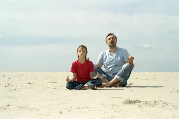 ヨガの練習を砂で遊ぶ息子とお父さん — ストック写真